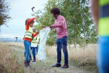 Adult Team Leader With Group Of Children At Outdoor Activity Camp Collecting Litter Together