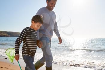 Father And Son Walking Along Beach By Breaking Waves On Beach With Fishing Net