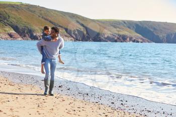 Loving Father Giving Son Piggyback As They Walk Along Winter Beach Together