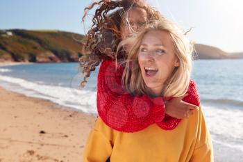 Loving Mother Giving Daughter Piggyback As They Walk Along Winter Beach Together