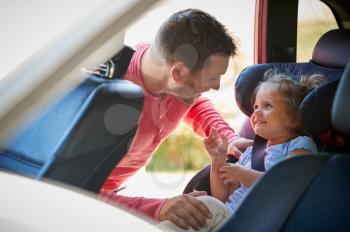 Father Securing Daughter Into Rear Child Seat Before Car Journey