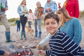 Multi-Generation Family Toasting Marshmallows Around Fire On Winter Beach Vacation