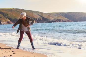 Senior Woman Skimming Stones Across Waves As She Walks Along Beach