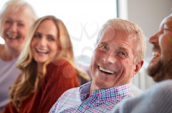 Senior Parents With Adult Offspring Sitting On Sofa At Home Talking And Laughing