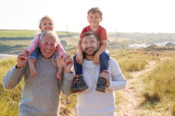 Portrait Of Grandfather And Father Giving Granddaughter And Son Ride On Shoulders At Beach