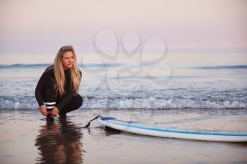 Female Surfer Wearing Wetsuit Attaching Surfboard Leash To Ankle In Waves
