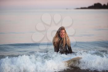Woman Wearing Wetsuit Sitting On Surfboard Riding Wave Into Beach
