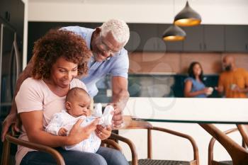 Grandparents Cuddling Baby Granddaughter At Home With Parents In Background