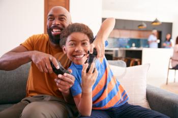 African American Father And Son Sitting On Sofa At Home Playing Video Game Together
