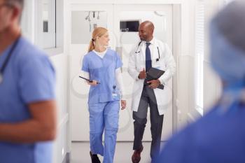 Doctor In White Coat And Nurse In Scrubs Having Discussion In Hospital Corridor