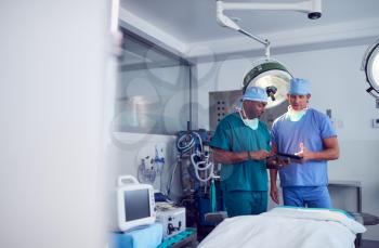 Male Surgeons Wearing Scrubs Looking At Digital Tablet In Hospital Operating Theater