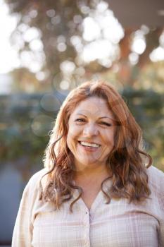 Portrait Of Smiling Senior Hispanic Woman In Garden At Home Against Flaring Sun