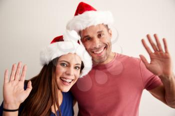 Portrait Of Hispanic Couple Wearing Santa Hats Celebrating Christmas Waving At Camera