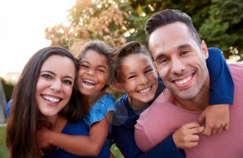 Portrait Of Smiling Hispanic Family With Parents Giving Children Piggyback Rides In Garden At Home
