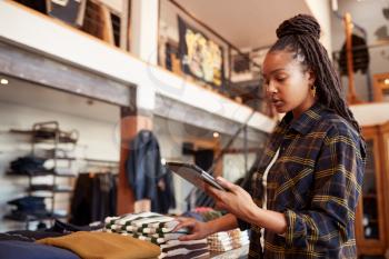 Female Owner Of Fashion Store Using Digital Tablet To Check Stock In Clothing Store