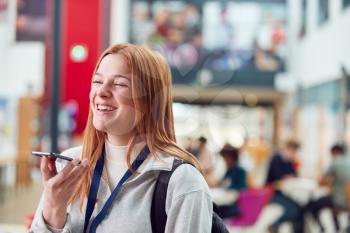 Smiling Female College Student Talking Into Mobile Phone In Busy Communal Campus Building