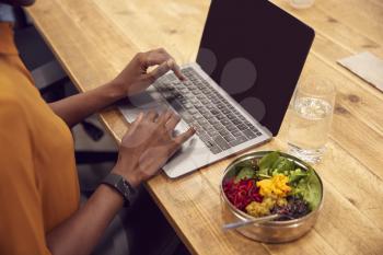 Close Up Businesswoman Working On Laptop Whilst Eating Vegan Lunch At Wooden Table