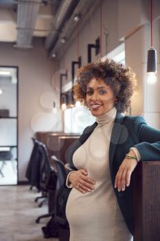 Portrait Of Pregnant Businesswoman Holding Bump Working In Modern Office
