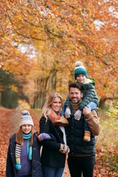 Portrait Of Family Walking Along Autumn Woodland Path With Father Carrying Son On Shoulders