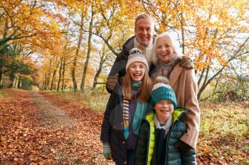 Portrait Of Grandparents With Grandchildren Enjoying Walk Along Autumn Woodland Path Together
