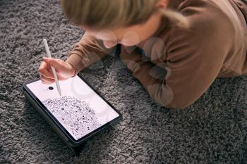 Close Up Of Woman Drawing On Digital Tablet Using Stylus Pen Lying On Carpet At Home