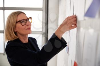 Mature Woman Looking At Designs On Wall In Start Up Fashion Business