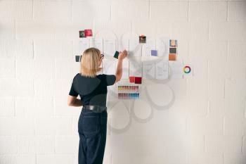 Rear View Of Mature Businesswoman Looking At Designs On Wall In Start Up Fashion Business
