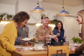 Group Of Mature Friends Meeting At Home Serving Food At Dinner Party And Drinking Wine Together