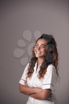 Studio Portrait Of Young Female Nurse Wearing Uniform Standing Against Grey Background