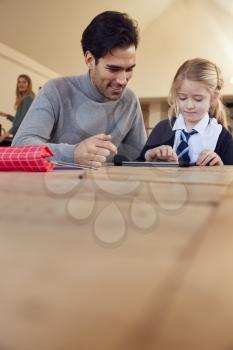 Father Helping Daughter Using Digital Tablet Wearing School Uniform With Homework At Table