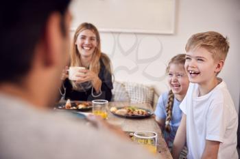 Family Sitting Around Table At Home In Pyjamas Enjoying Brunch Together