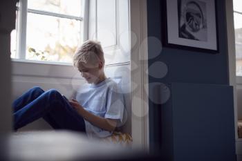 Young Boy Sitting On Window Seat At Home Playing On Digital Tablet