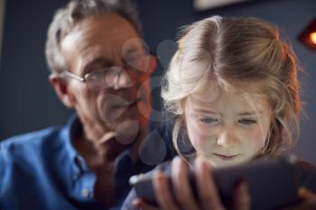 Close Up Of Granddaughter With Grandfather In Chair Looking At Digital Tablet At Home Together