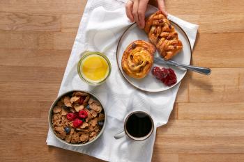 Overhead Flat Lay Of Woman Eating At Table Laid For Breakfast With Cereal Croissant And Pastries