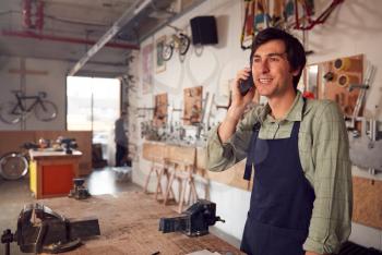 Male Business Owner In Workshop Making Call On Mobile Phone