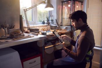 Male Jeweller Looking At Ring Design On Digital Tablet In Studio