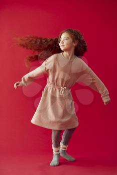 Girl With Long Red Hair Spinning Around Against Red Studio Background
