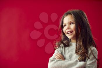 Portrait Of Young Girl With Folded Arms Against Red Studio Background Smiling At Camera