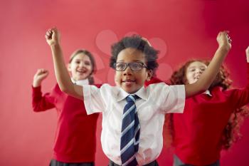 Group Of Excited Elementary School Pupils Wearing Uniform Having Fun Against Red Studio Background