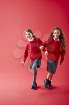 Two Elementary School Pupils Wearing Uniform Linking Arms Against Red Studio Background