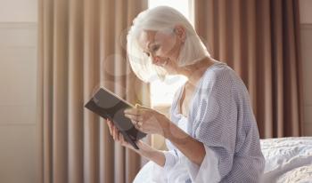 Smiling Senior Woman Sitting On Edge Of Bed Looking At Photo In Frame