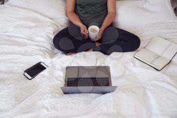 Close Up Of Businesswoman Sitting On Bed With Laptop And Diary Working From Home