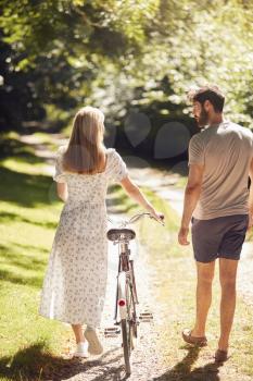 Rear View Of Couple Walking Along Summer Countryside Path Pushing Bike