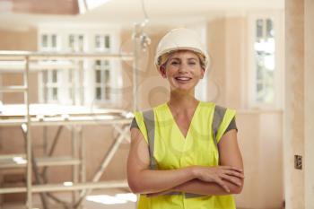 Portrait Of Smiling Female Builder Wearing Hard Hat Working In New Build Property