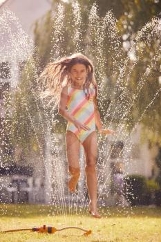Girl Wearing Swimming Costume Having Fun In Summer Garden Playing In Water From Garden Sprinkler