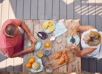 Overhead Shot Of Retired Couple Outdoors On Deck At Home Eating Breakfast