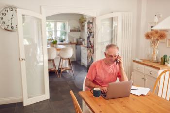 Retired Man On Phone At Home In Kitchen Using Laptop