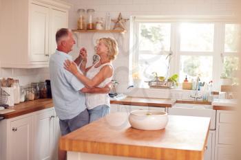 Retired Romantic Couple Dancing In Kitchen At Home Together
