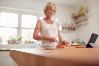Retired Woman Making Meal In Kitchen With Smart Speaker In Foreground