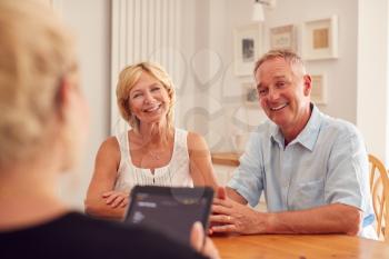 Retired Couple Meeting With Female Financial Advisor In Kitchen At Home